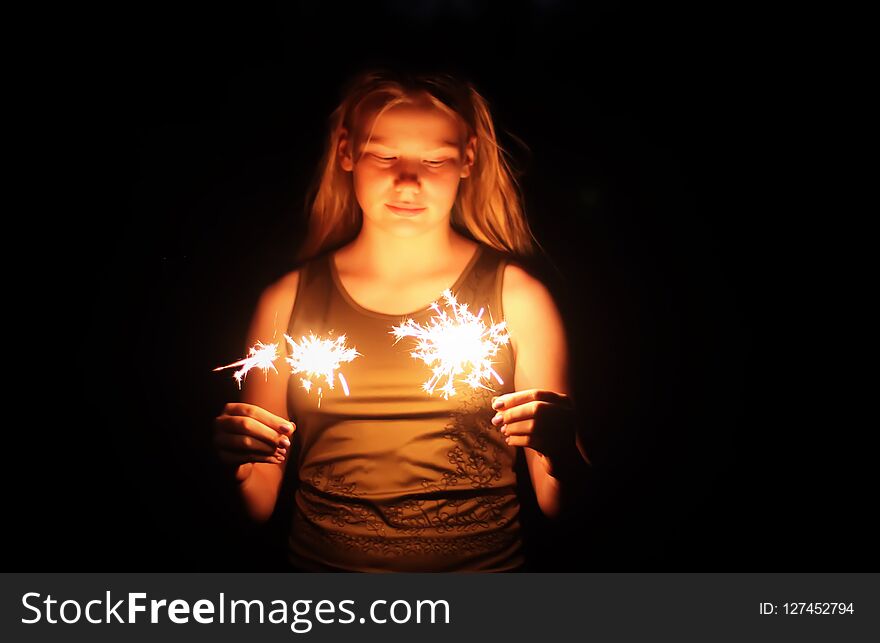 Teenager girl holding a burning sparklers in her hands on night darkness background. Teenager girl holding a burning sparklers in her hands on night darkness background.