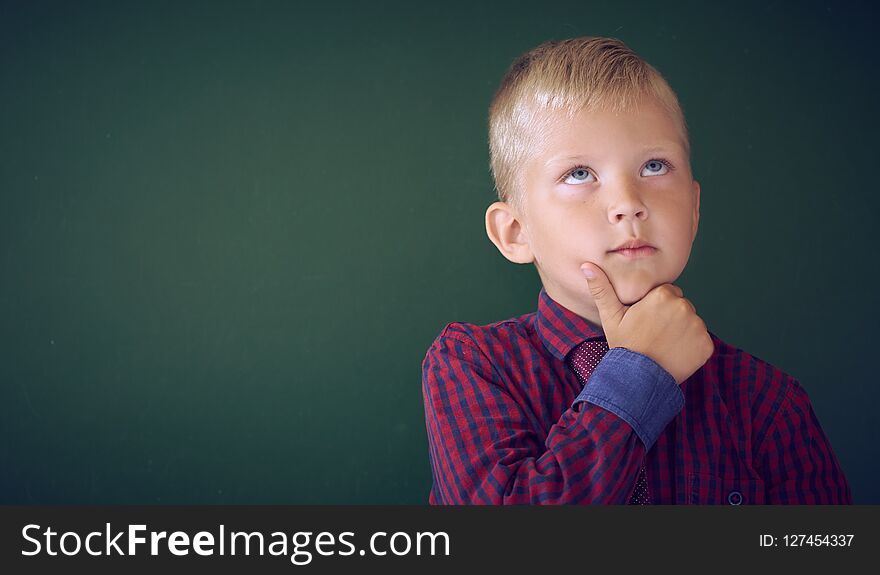 Closeup Shot Of Schoolboy Thinking With Hand On Chin Isolated On Blackboard. Portrait Of Pensive Child Thinking About