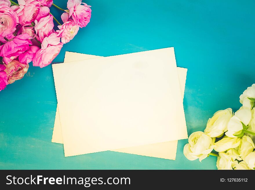 Pink and white ranunculus flowers on blue wooden background with copy space on blank paper notes, retro toned