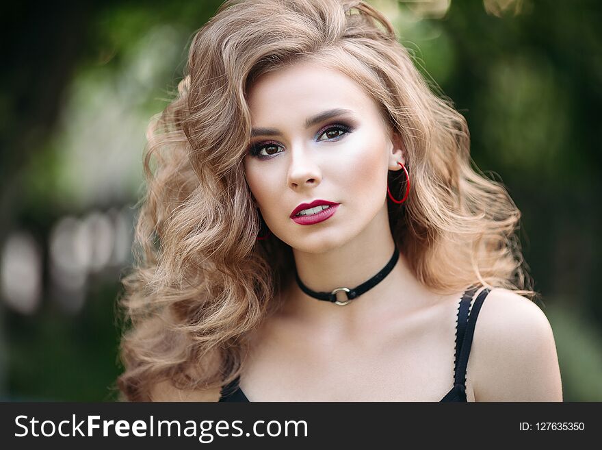 Portrait of a beautiful blonde girl. Women with makeup and beautiful wavy hair in a black T-shirt. In a city park on a green background. Close-up. Portrait of a beautiful blonde girl. Women with makeup and beautiful wavy hair in a black T-shirt. In a city park on a green background. Close-up.