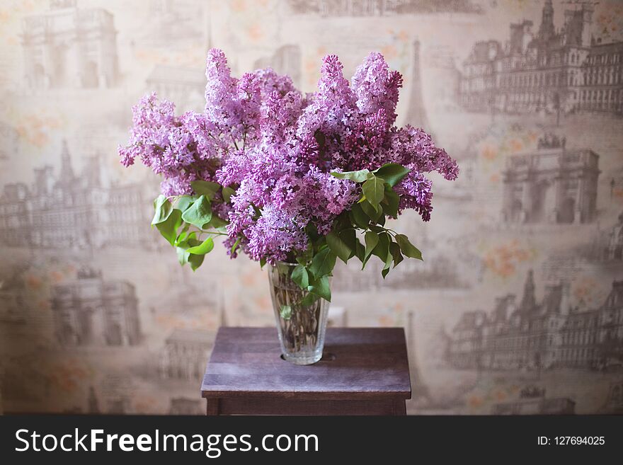 Beautiful large bouquet of lilacs in a glass vase on a wooden stand. Beautiful large bouquet of lilacs in a glass vase on a wooden stand