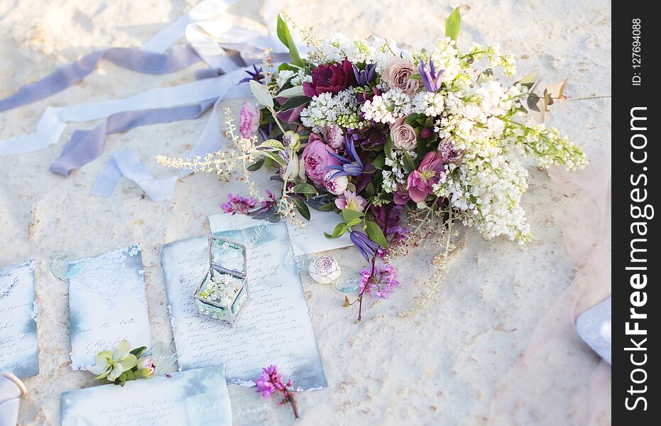 Incredible bridal bouquet of white lilac roses with ribbons on the white rocky shore. Incredible bridal bouquet of white lilac roses with ribbons on the white rocky shore