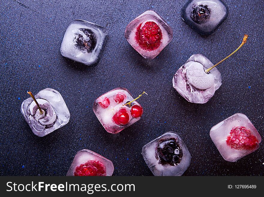 Frozen berries raspberries, blackberries, blueberries, red currant, cherry in ice cube over white fabric background. Top view.