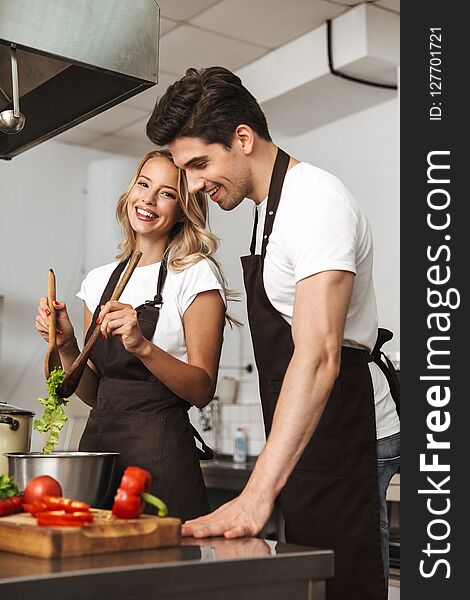 Smiling excited young friends loving couple chefs on the kitchen cooking.