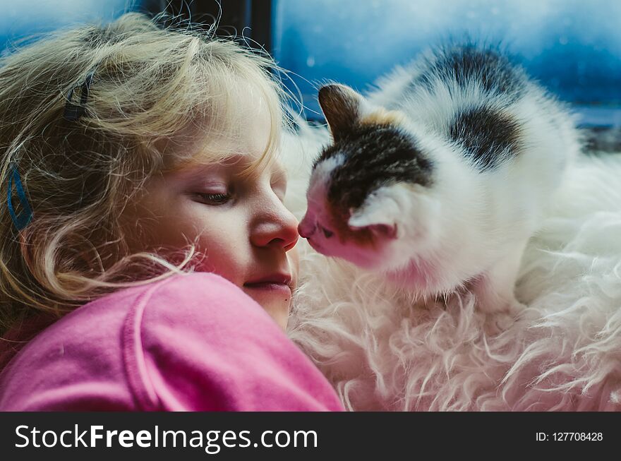 Lovely blond girl and a cat by the window looking into eyes in winter time. Lovely blond girl and a cat by the window looking into eyes in winter time