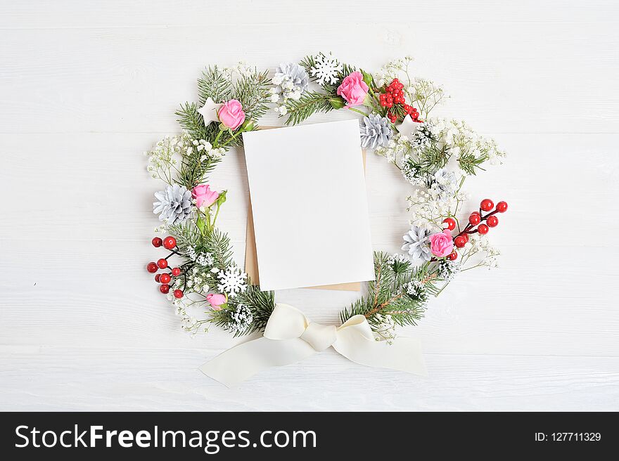 Mockup Of Christmas Wreath With Sheet Of Paper Decorated With Red Berries, Cones And Roses. On Wooden Background