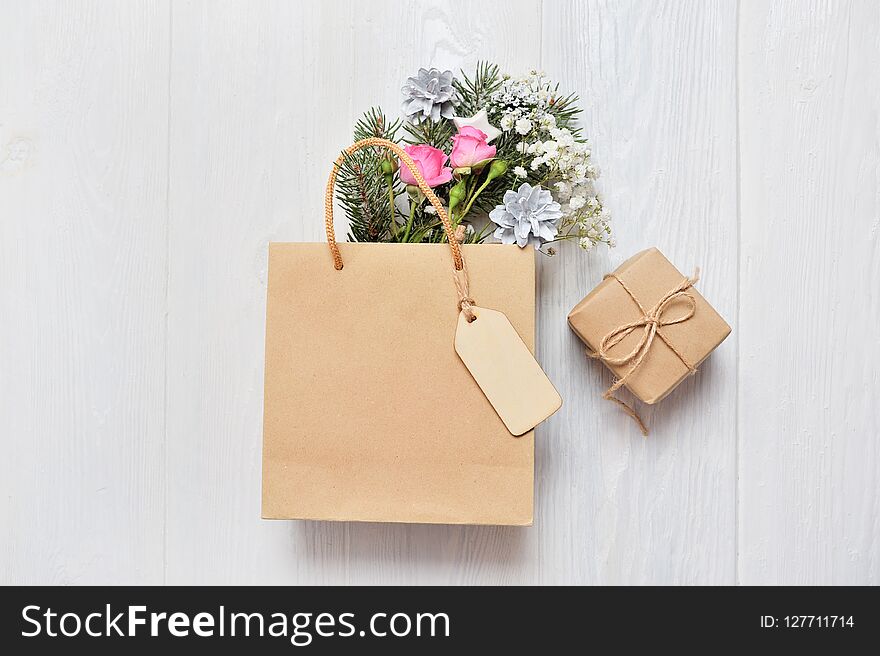 Christmas mockup shopping concept. Kraft package with wooden tag and xmas decor fir branches, pink roses, cones with place for you