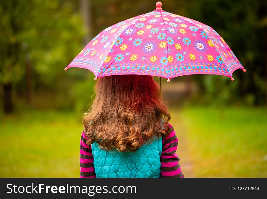 Beautiful Russian Little Girl With Wavy Brown Hair Under Colorful Umbrella In Autumn Park Rear View. Beautiful Russian Little Girl With Wavy Brown Hair Under Colorful Umbrella In Autumn Park Rear View.