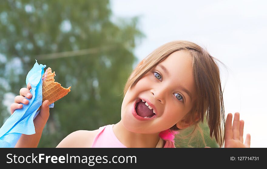 Pretty little girl eating licking big ice cream in waffles cone and grimacing happy laughing on nature background. Favorite treat on a hot summer day for kids. Pretty little girl eating licking big ice cream in waffles cone and grimacing happy laughing on nature background. Favorite treat on a hot summer day for kids.