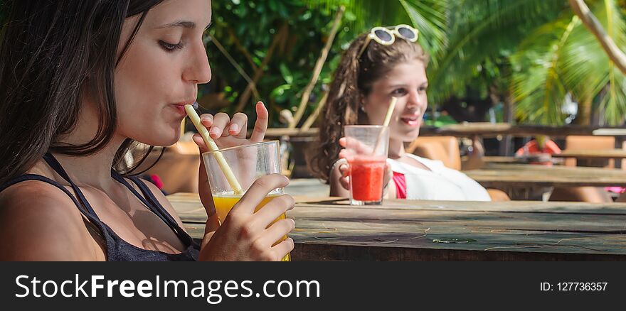 Two girlfriends sitting in bar cafe, drinking fruit cocktail on a tropical beach. Two girlfriends sitting in bar cafe, drinking fruit cocktail on a tropical beach