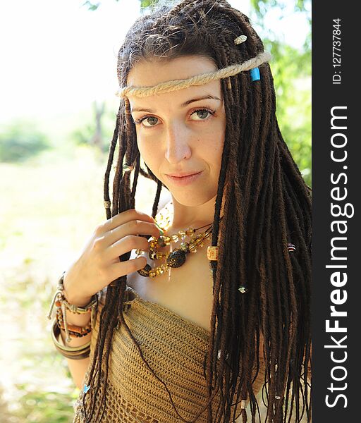 Beautiful boho style woman with dreadlocks portrait, looking at camera, against sunny summer
