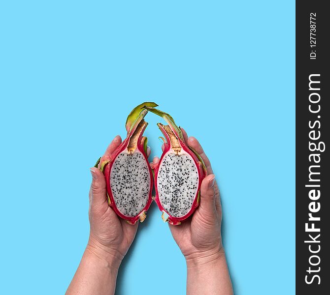Halves of an organic exotic fruit pitahaya hold the woman`s hands on a blue background with space for text. Flat lay. Halves of an organic exotic fruit pitahaya hold the woman`s hands on a blue background with space for text. Flat lay