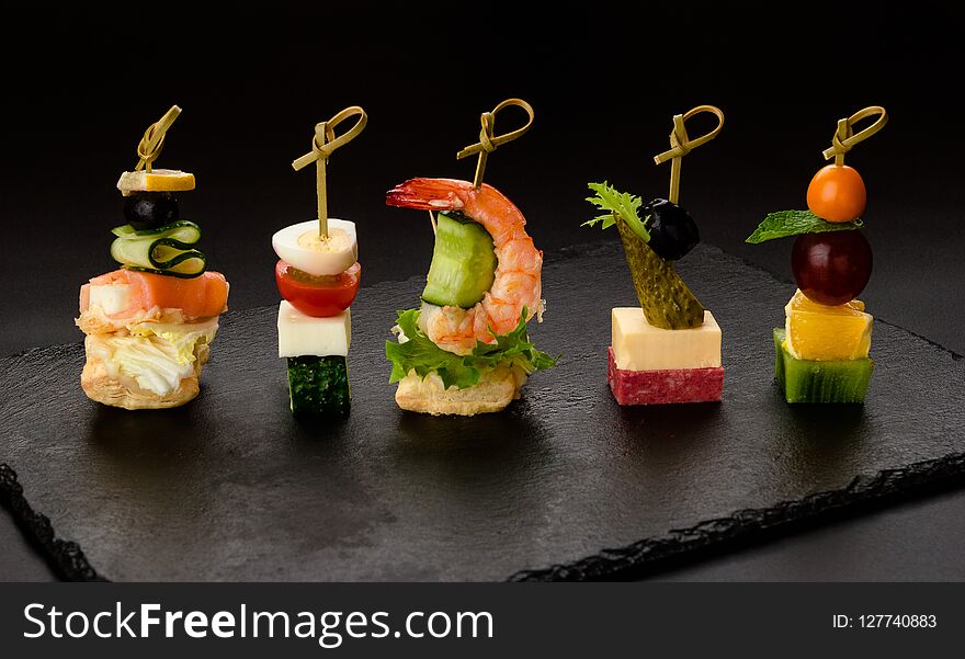 Different kind of snaks, small canape with cherry tomatoes, cheese, sausages, vegetables and fruits on skewers.