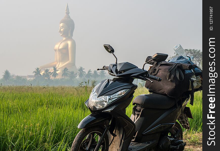 Large sitting Buddha above the palm trees and rice fields with scooter on foreground. The biggest Buddha of Thailand. Ang Thong province, Thailand. Bike backpacker Travel Concept