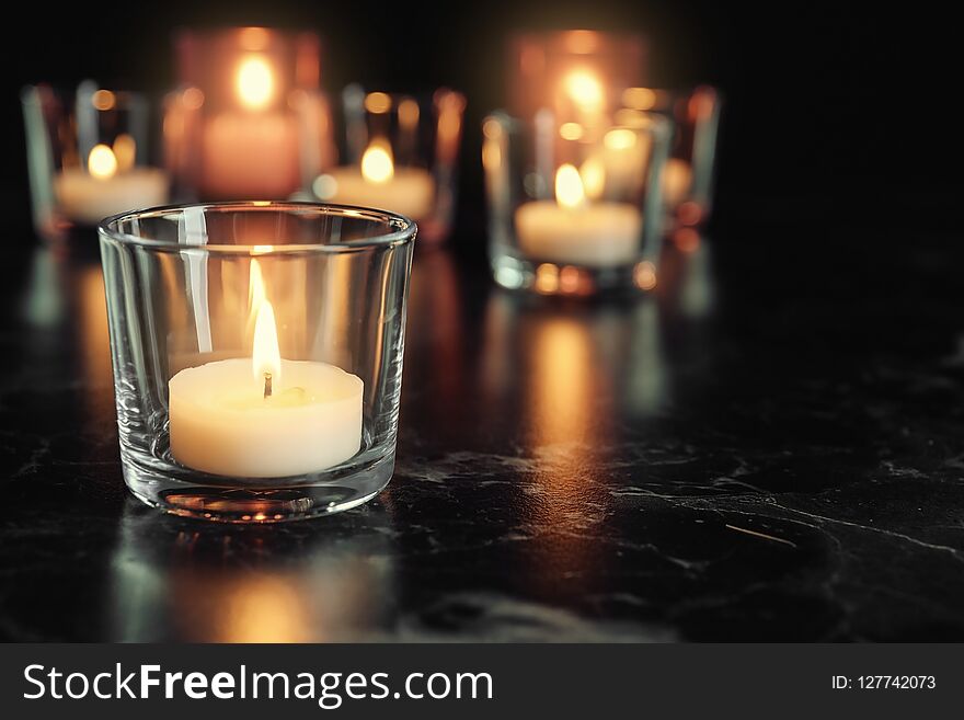 Burning candle on table in darkness, space for text. Funeral symbol