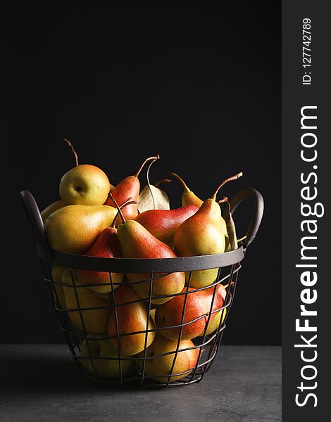 Basket with ripe pears on table against black background
