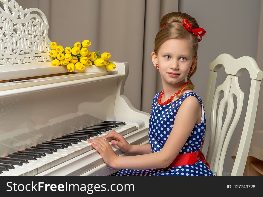 A sweet schoolgirl girl sits beside a white grand piano on which lies a bouquet of flowers. The concept of studying music, spring mood, happy people. A sweet schoolgirl girl sits beside a white grand piano on which lies a bouquet of flowers. The concept of studying music, spring mood, happy people.