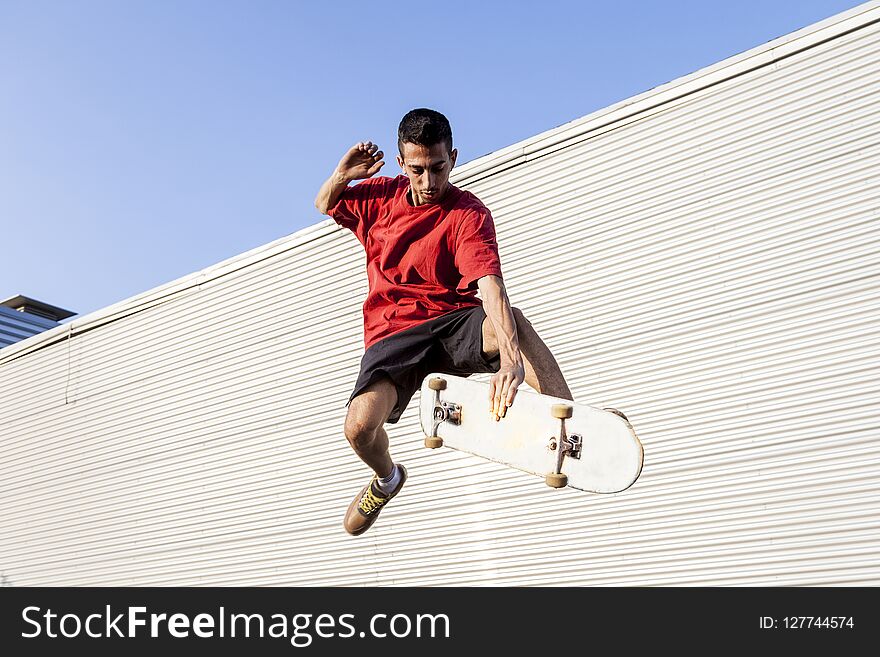 Young skateboarder jumps up with his board in front of a metal background on the roofs of an abandoned building