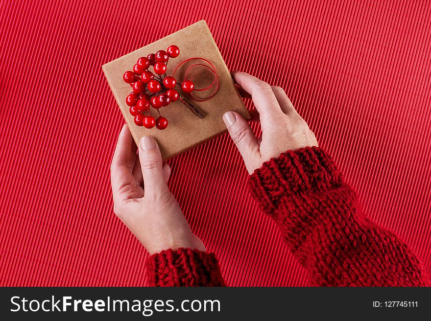 Female hands holding the gift box with Christmas decoration, bright red background