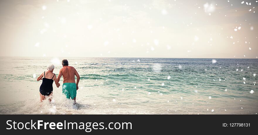 Snow falling against rear view of senior couple holding hands and walking in sea. Snow falling against rear view of senior couple holding hands and walking in sea