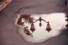 Interesting Reflection Of A Lantern In A Puddle In A Hole On The Afalt With A Crack In The Light Of The Setting Sun. Stock Photo Interesting Reflection Of A Lantern In A Puddle In A Hole On The Afalt With A Crack In The Light Of The Setting Sun. Stock Photo