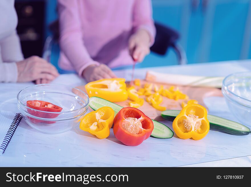 Tasty vegetables. Young person standing near the kitchen table and carefully cutting vegetables while cooking. Tasty vegetables. Young person standing near the kitchen table and carefully cutting vegetables while cooking