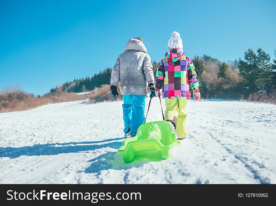 Little boy and girl carry the sled and enjoying winter sledding time