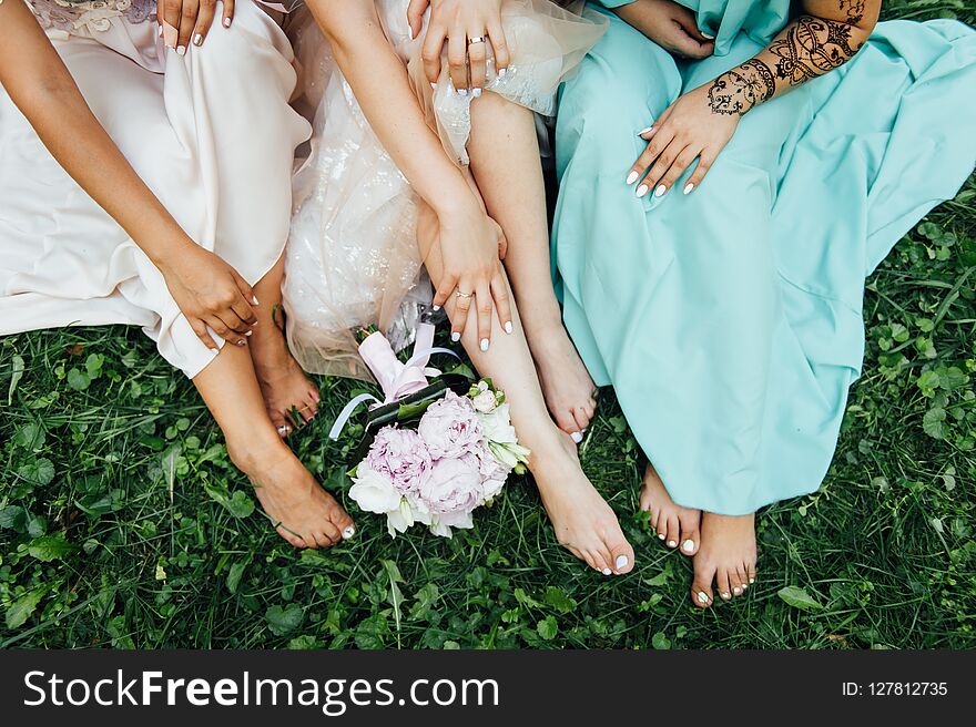 Feet of the bride and her bridesmaids on the green grass in summer time