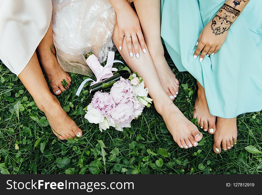 Feet of the bride and her bridesmaids on the green grass in summer time