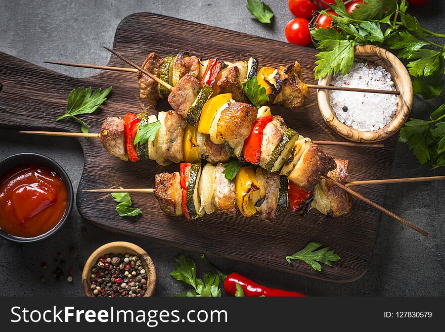 Grilled shish kebab or shashlik with vegetables on black stone table. Pork meat. Barbeque meat dish. Top view. Grilled shish kebab or shashlik with vegetables on black stone table. Pork meat. Barbeque meat dish. Top view.