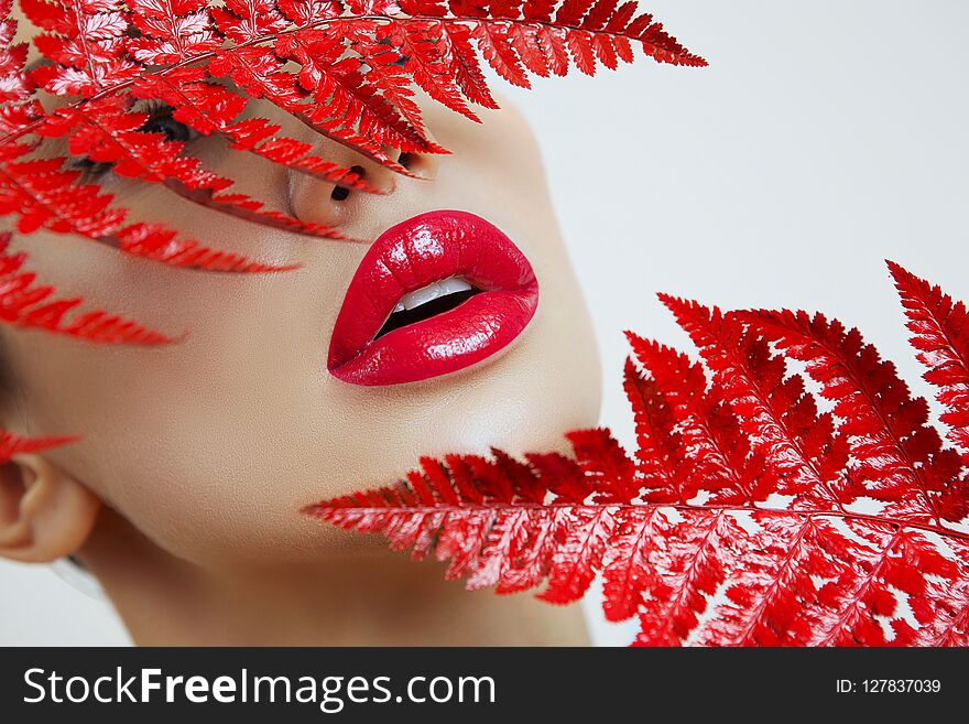 A woman with Sensual red lips and a fern. Woman`s mouth with red Lips. woman Red Lips on a Gray background. Female portrait with bright makeup. Lip gloss