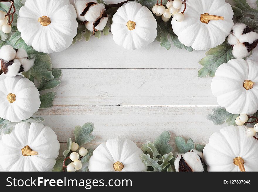 Autumn frame of white pumpkins and leaves over rustic white wood