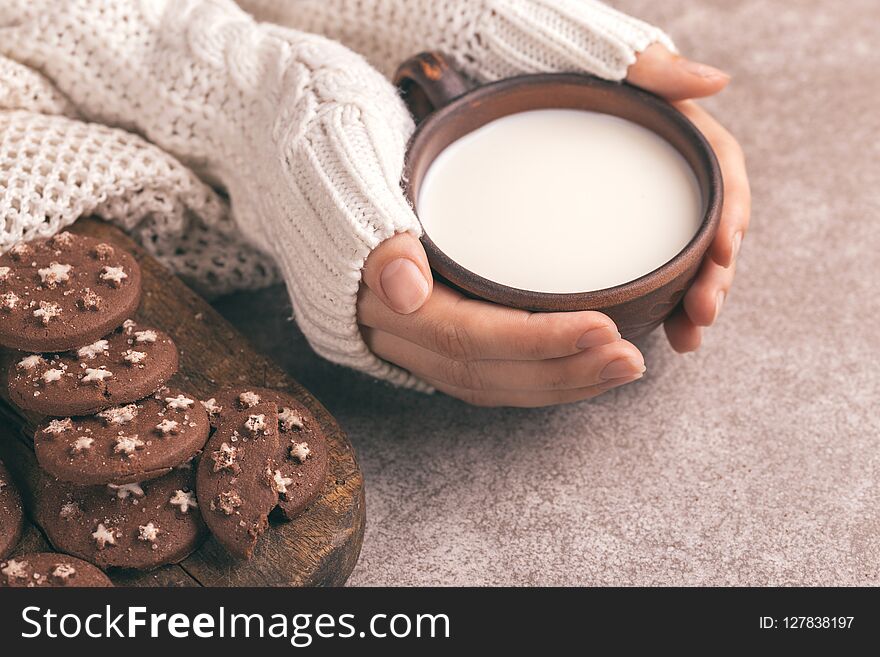 Female hands are holding cup of warm milk, chocolate cookies on