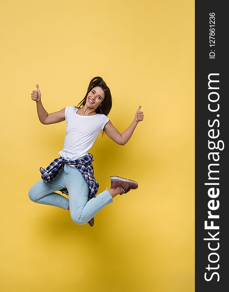 Full length portrait of a cheerful casual caucasian woman jumping isolated over yellow background.