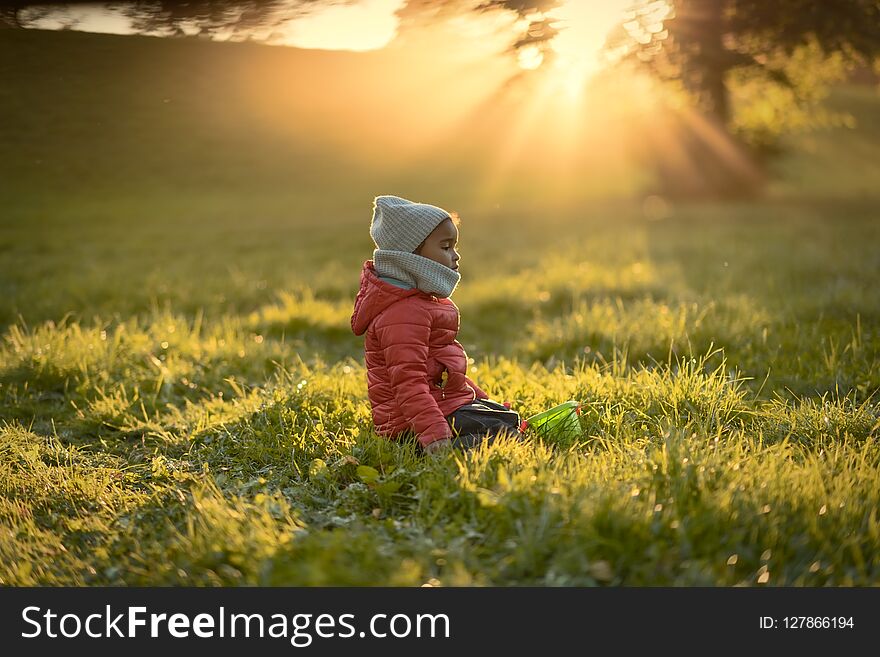 A Child In The Rays Of A Warm Sun Sitting On The Grass.