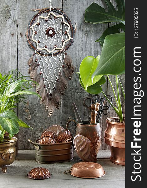 Dream catcher and vintage copper molds in interior on wooden gray background. Green plants and copy space for text. Dream catcher and vintage copper molds in interior on wooden gray background. Green plants and copy space for text.