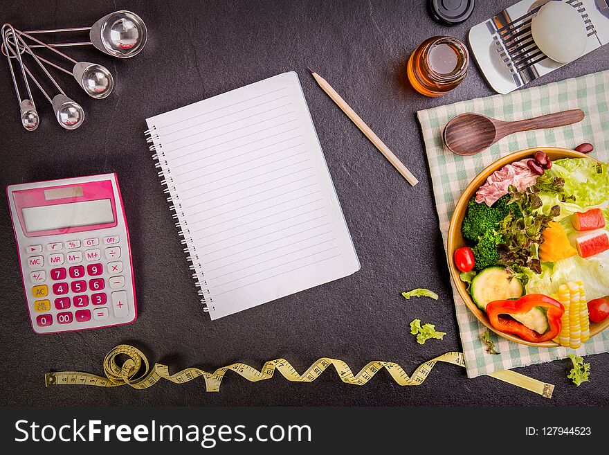 The Dieting and nutrition. Diet plan, tape measure, calculator for Count calories, salad healthy food on black stone background. Weight loss. Copy space.