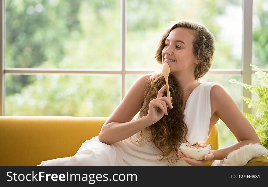 Healthy young woman lying on a couch holding a bowl of yogurt looking relaxed and comfortable