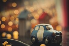 Blue And White Cute Cartoon Car On Orange Bokeh Background. Used Car Concept. Toy Car Model. Car Toy Model Parked In Town At Night Stock Image