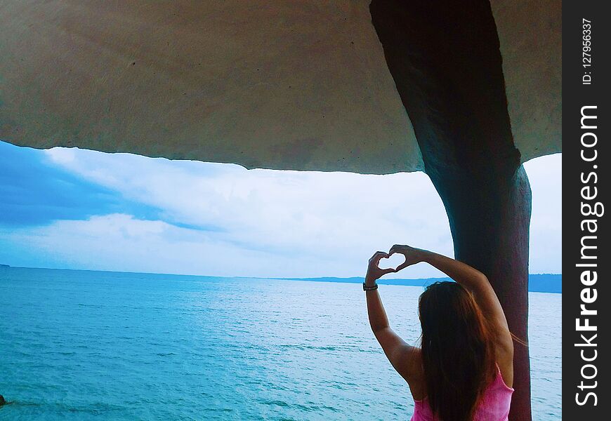 a lady showing heart symbol using her hands while facing the ocean. a lady showing heart symbol using her hands while facing the ocean