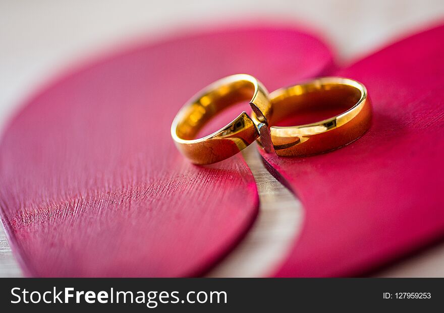 Two broken golden wedding rings on broken red heart. Divorce concept