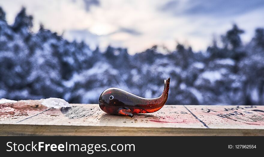 Winter background. Glass whale toy in front of forest covered with snow.