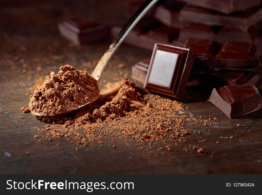 Broken chocolate pieces and cocoa powder in small spoon on a wooden background. Broken chocolate pieces and cocoa powder in small spoon on a wooden background.