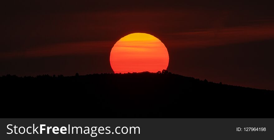 Panoramic sunrise over mountain peak with huge orange sun