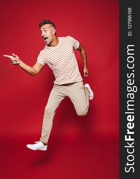 Full length photo of adult man in striped t-shirt running and screaming isolated over red background