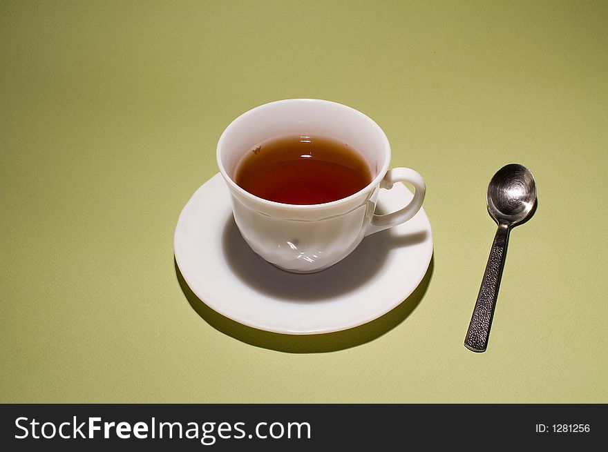 White cup of tea on plate with spoon beside.