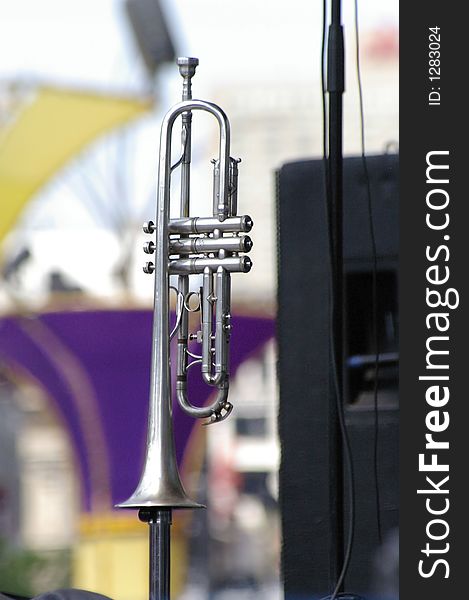 A silver trumpet sitting on a stand on stage at an outdoor jazz festival. A silver trumpet sitting on a stand on stage at an outdoor jazz festival