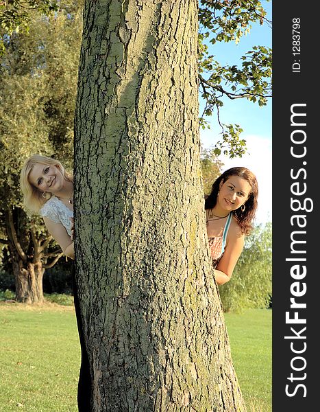 Two girls peeking from behind a tree on a sunny afternoon. Two girls peeking from behind a tree on a sunny afternoon