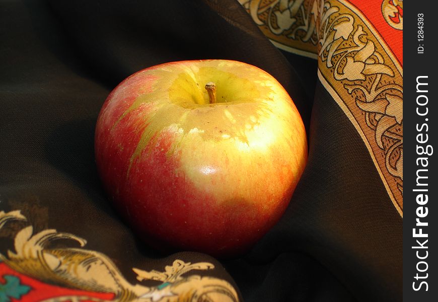 Delicious apple pretty. Yellow-red apple on a background of a black scarf with a yellow-red  ornament. Delicious apple pretty. Yellow-red apple on a background of a black scarf with a yellow-red  ornament