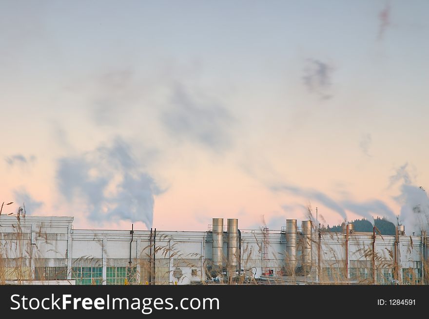 Factory belching out smog from its smokestacks lit by the evening light